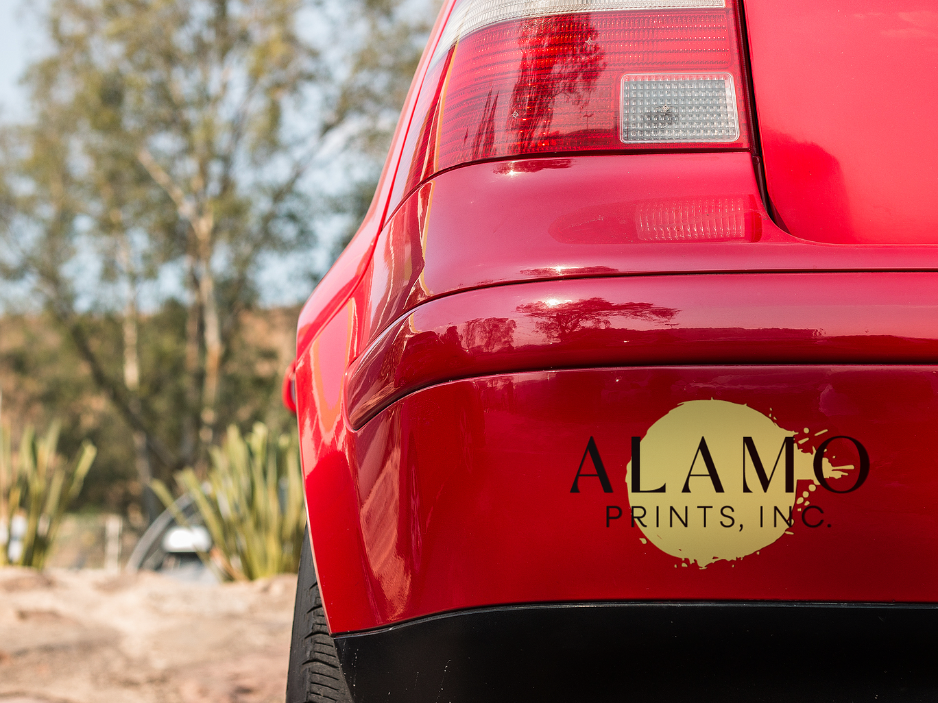 Red car with Alamo Prints logo, outdoor setting.
