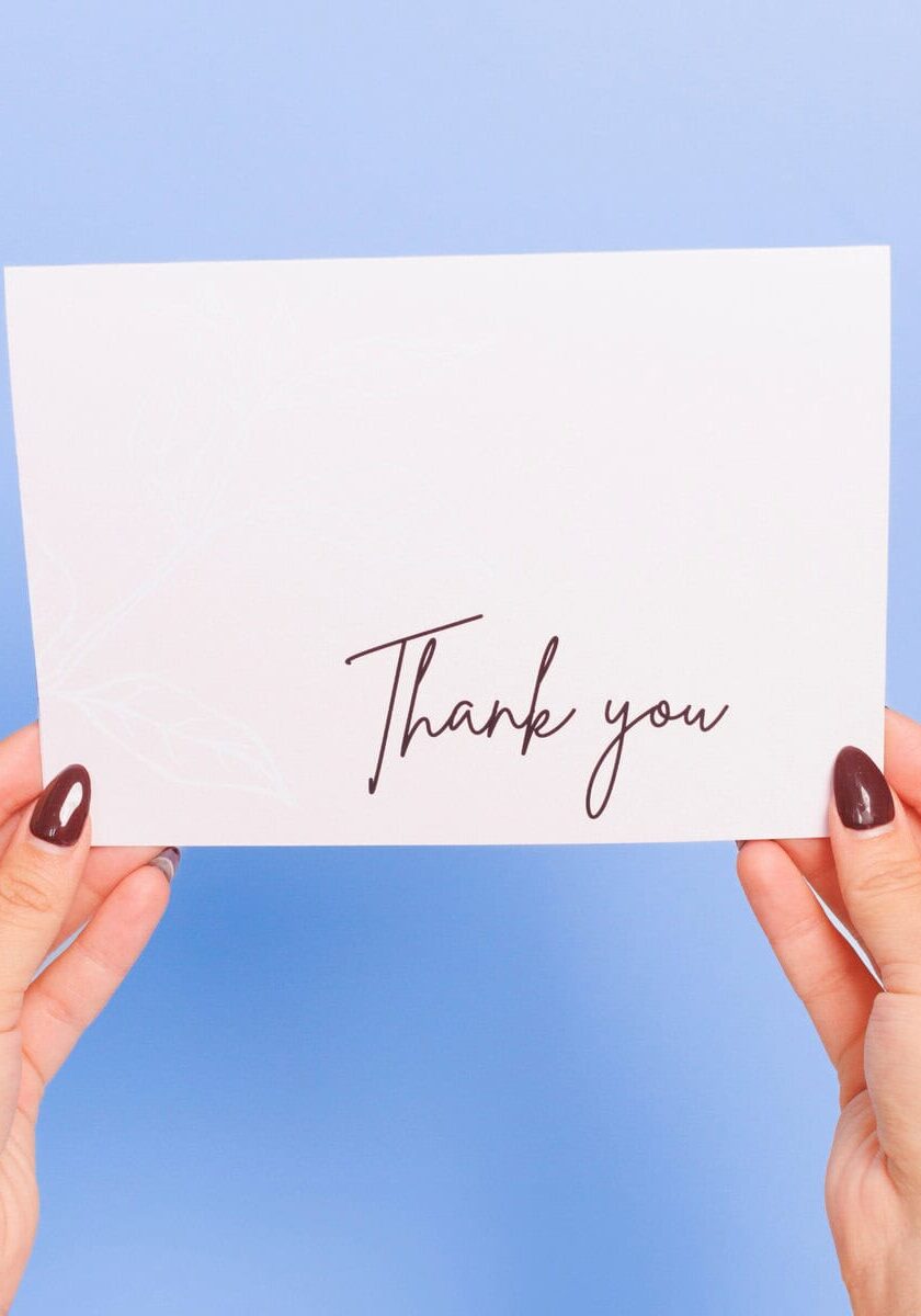 Hands holding thank you card on blue background.